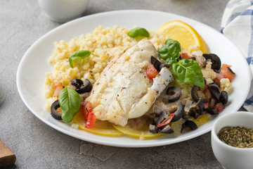 Baked white fish fillet (Pollock, cod, sea bass, Dorada) with olives, tomatoes and lemon. Traditional French food, bulgur