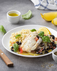 Baked white fish fillet (Pollock, cod, sea bass, Dorada) with olives, tomatoes and lemon. Traditional French food, bulgur