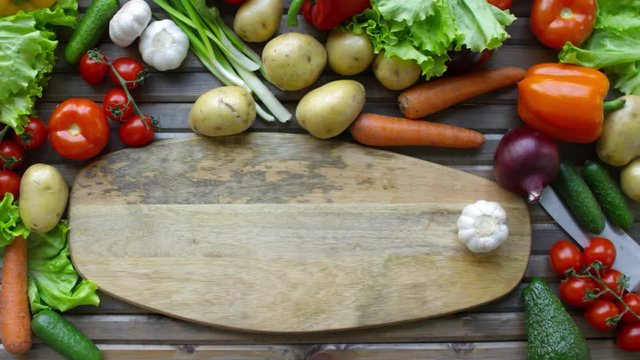 Top view of hands of unrecognizable male cook sliding bulb of garlic on wooden cutting board with copy space while preparing food on kitchen table with lots of fresh vegetables around