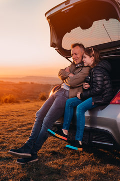 Father And Daughter Enjoying Sunset While Sitting In The Car Trunk