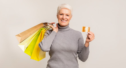 Pleased elderly woman holding credit card and colorful shopping bags