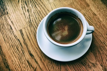 White Cup of Black Coffee on the Wooden Table in Classic Tone.