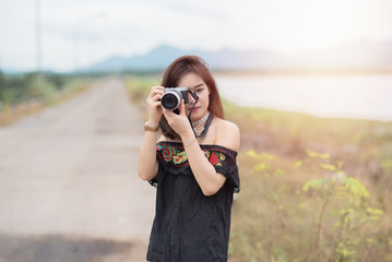 Young asian female photographer with camera outdoors at the park. Thai woman holding camera in hand.