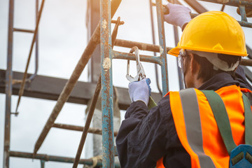 [safety body construction] Working at height equipment. Fall arrestor device for worker with hooks for safety body harness on selective focus. Worker as in construction background. - obrazy, fototapety, plakaty