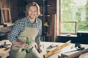 Portrait of his he nice attractive handsome blond cheerful cheery guy wearing checked shirt uniform sitting on desk having rest time at industrial brick loft style interior studio indoors