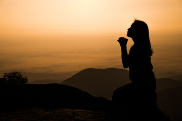 Silhouette of woman kneeling and praying over beautiful sunrise background - obrazy, fototapety, plakaty