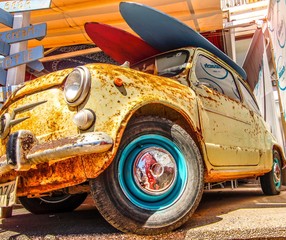 rusty old beach Mini Cooper with surfboards on the roof