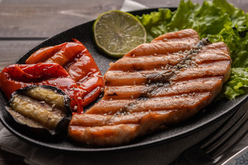 Homemade grilled salmon steak on lettuce leaves on the plate. Next to baked vegetables, lime. Healthy food