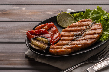 Homemade grilled salmon steak on lettuce leaves. On a plate on a linen napkin. Next to baked vegetables, soy sauce, lime. Close up