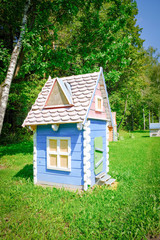 A wooden fairy-tale toy house in green grass in the sun. The concept of 