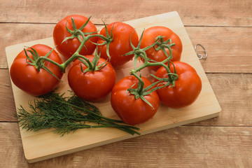Tomatoes lie on a cutting board. Nearby lies a green dill.