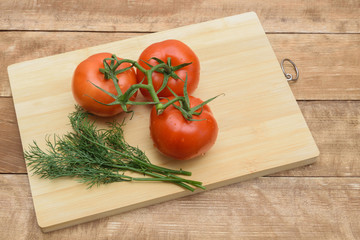 Tomatoes lie on a cutting board. Nearby lies a green dill.