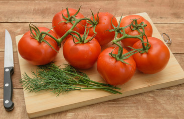 Tomatoes lie on a cutting board. Nearby lies a green dill.