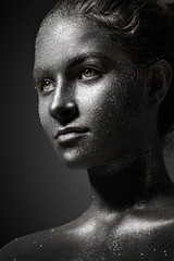 the girl's beautiful face is painted silver with sequins. shiny metal powder particles sparkle on the model's face