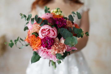 the bride holds a wedding bouquet of red and pink flowers indoor young girl in a white dress and red hair with a delicate festive  bouquet  roses in hands stylish flower composition of bright roses