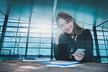 Smiling business woman sitting using smartphone with documents on table and airport terminal background, Double exposure