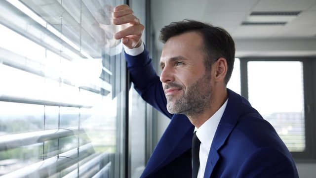 Handsome businessman walking leaning on office window looking out and smiling