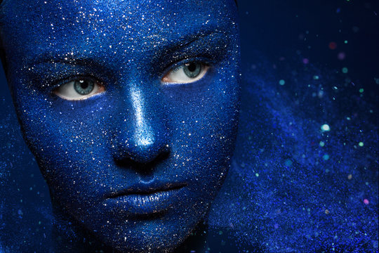 beautiful girl face vakrasana blue paint with glitter. The effect of the collapse. the flying particles of powder