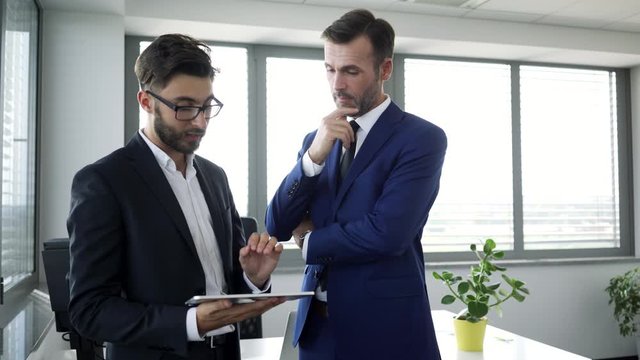 Young businessman showing project advancements to boss and talking with him in office