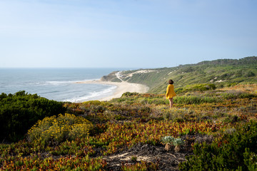 Girl view from the back and side standing on the grass with a view to the beach from the top of a mountain.