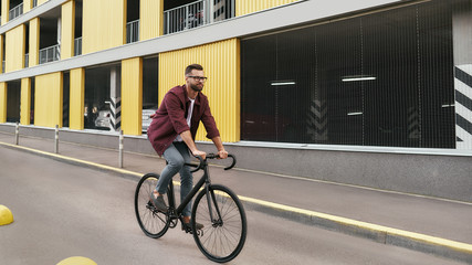 Bike Everywhere. Side view of handsome man with stubble in casual clothes riding on his bicycle...
