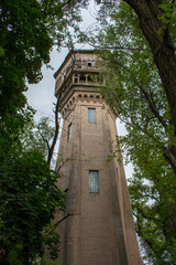 Obraz premium Abandoned tower in forest. Old wooden and brick building. Vintage architecture. Desolation concept. Retro house with wooden balcony. Facade of ruined high tower.