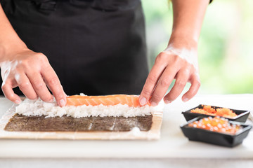 Chef preparing sushi. Asian woman chef in black uniform, putting raw salmon on rice, close up.