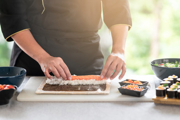 Chef preparing sushi. Asian woman chef in black uniform, putting raw salmon on rice, tidy up rice with light leaks.