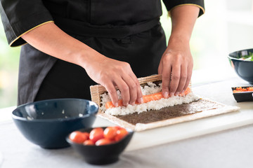 Obraz na płótnie Canvas Chef preparing sushi. Asian woman chef in black uniform, about to roll salmon into sushi.