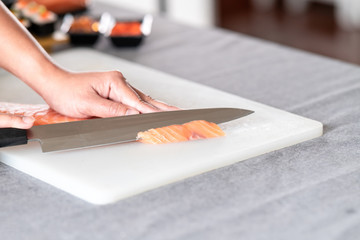 Chef slicing raw salmon on plastic plate. Asian woman chef in black uniform, slicing small piece of...