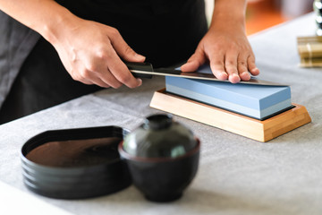 Chef sharpening knife on table. Japanese setting with asian woman. Side shot.