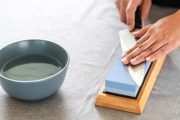 Chef sharpening knife on table. Japanese setting with asian woman. With water bowl.