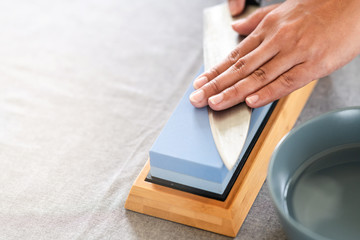 Chef sharpening knife on table. Japanese setting with asian woman. With water bowl.