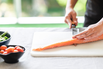 Chef prepare to cut raw salmon. Asian woman chef in black uniform, slicing halfway of raw salmon..