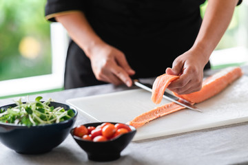 Chef prepare to cut raw salmon. Asian woman chef in black uniform, cutting skin of salmon.