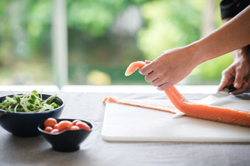 Chef prepare to cut raw salmon. Asian woman chef in black uniform, cutting skin of salmon with green background.