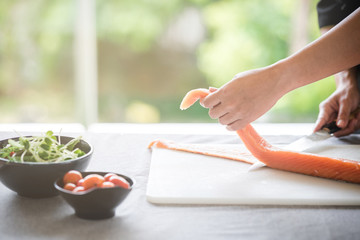 Chef prepare to cut raw salmon. Asian woman chef in black uniform, cutting skin of salmon with green background with light leaks.