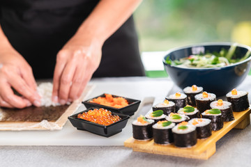 Chef preparing sushi. Asian woman chef in black uniform, putting rice on nori seaweed, with salmon...