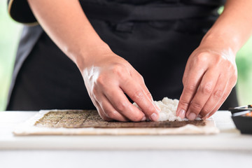 Chef preparing sushi. Asian woman chef in black uniform, putting rice on nori seaweed and making shape, close up.