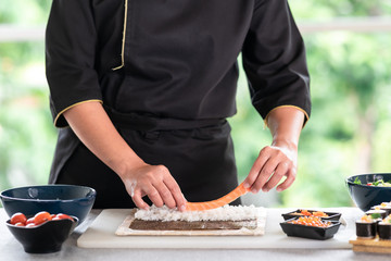 Obraz na płótnie Canvas Chef preparing sushi. Asian woman chef in black uniform, putting raw salmon on rice.