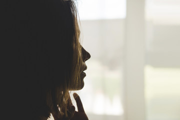 Silhouette of girl at window of clasped hand in gesture of prayer.