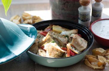 On a natural wood table in a ceramic bowl lies baked fish with vegetables and spices. Homemade food.