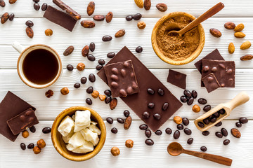 Chocolate bars and nuts on white wooden table background top view