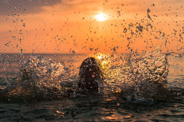 A girl and a water splash with a sunset on the background