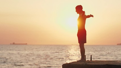 Young man jumping from sea pier and doing frontflip during beautiful sunrise, slow motion