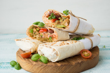 Traditional Mexican food burritos with beans and vegetables. Vegetarian rolls with red beans and vegetables lie on an aged wooden table.