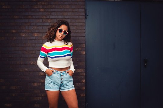 Curly haired woman with colored sunglasses infront of brick wall