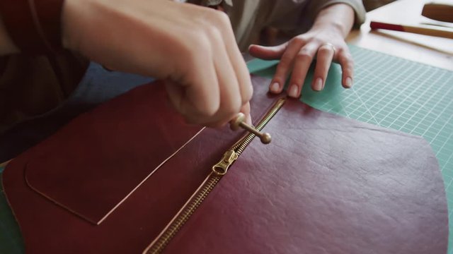 Close up of artisan hands holding special steel tool and gluing zipper and piece of brown raw leather
