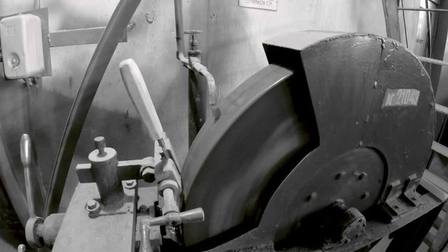 An old machine for sharpening tools and chisels. Large abrasive stone. On top of the tap and water flows for lubrication. It rotates slowly. The chisel is fixed in the clamp.Monochrome color. 4 K.