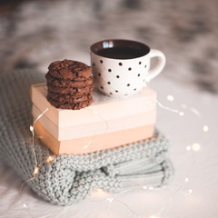 Winter holidays concept. Hot tea with tasty chocolate cookies with knitted sweater and books over Christmas lights at background. Night time. Good morning.